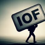 Silhueta de uma pessoa curvada carregando nas costas uma enorme placa metálica com as letras “IOF”, simbolizando o peso financeiro do imposto sobre o contribuinte. A imagem transmite o impacto negativo do IOF na vida do cidadão e seu papel em medidas de ajuste fiscal controversas.