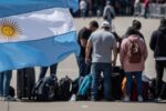 Bandeira da Argentina em destaque em primeiro plano, com grupo de turistas brasileiros desanimados e bagagens ao fundo, simbolizando o alto custo das viagens para a Argentina e o impacto econômico para os brasileiros.